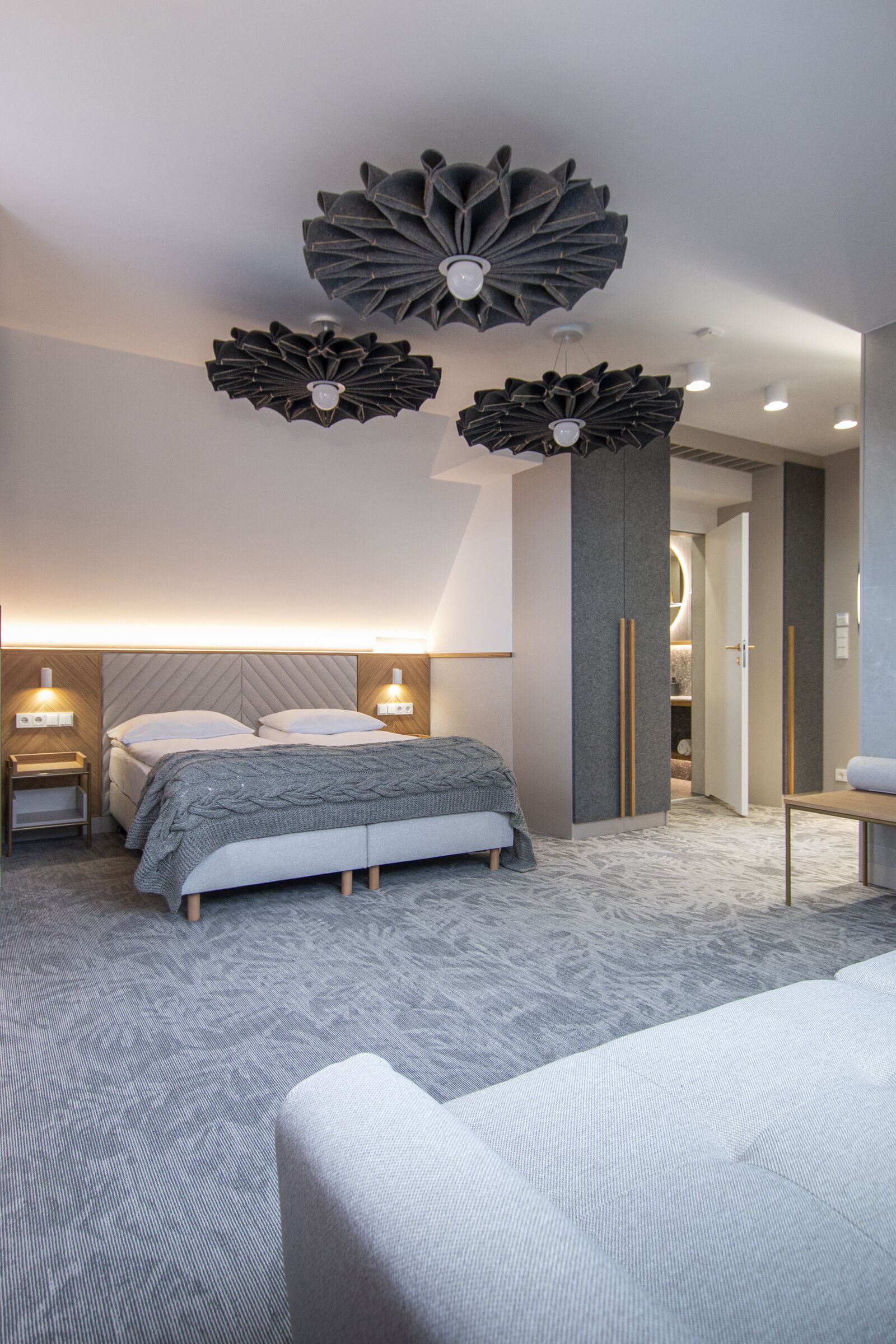 Quarto moderno com uma cama grande, mesas de cabeceira e uma luminária de teto singular.