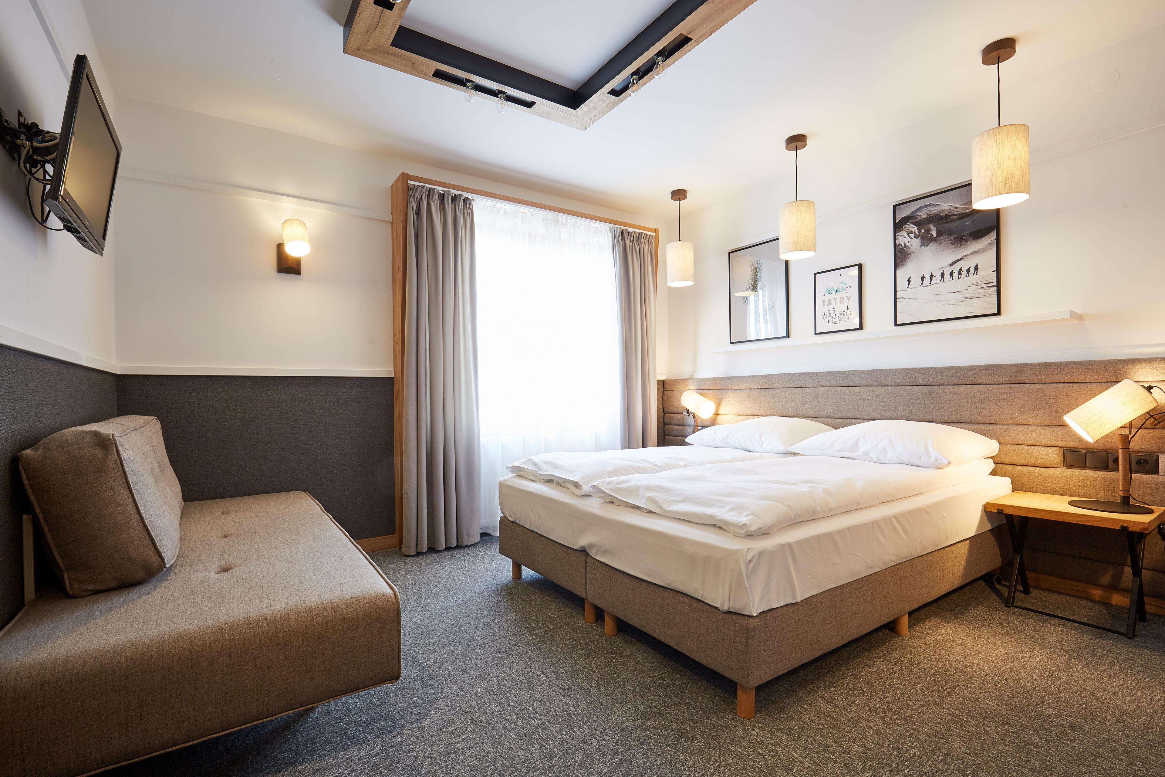 Quarto de hotel moderno com cama, sofá, escrivaninha e televisão de tela plana.