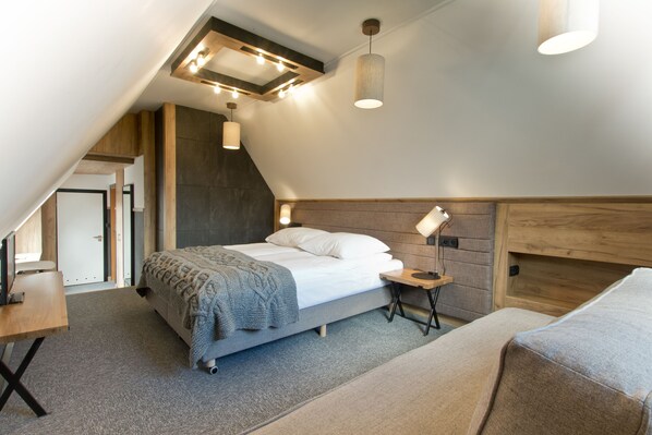 A modern bedroom with a sloped ceiling, a bed with a wooden headboard, a bedside table with a lamp, and a small desk with a chair. - Pensjonat Tatry (Koscielisko)