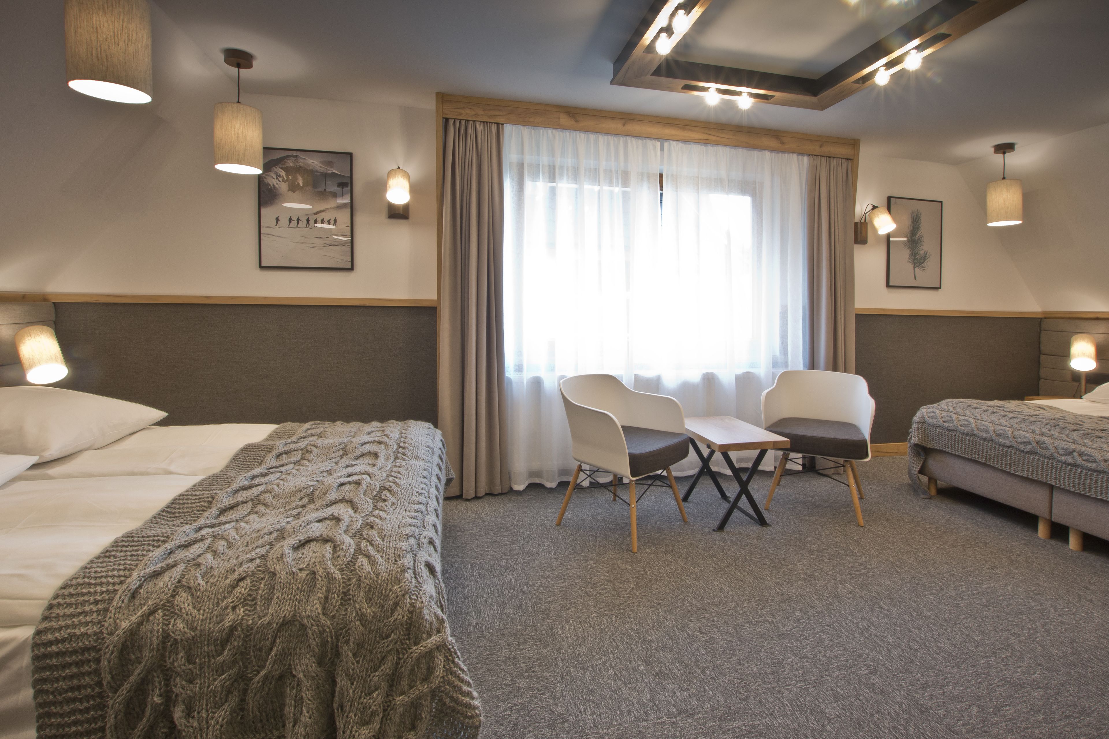 A hotel room with a bed, two chairs, a small table, and a window with curtains.