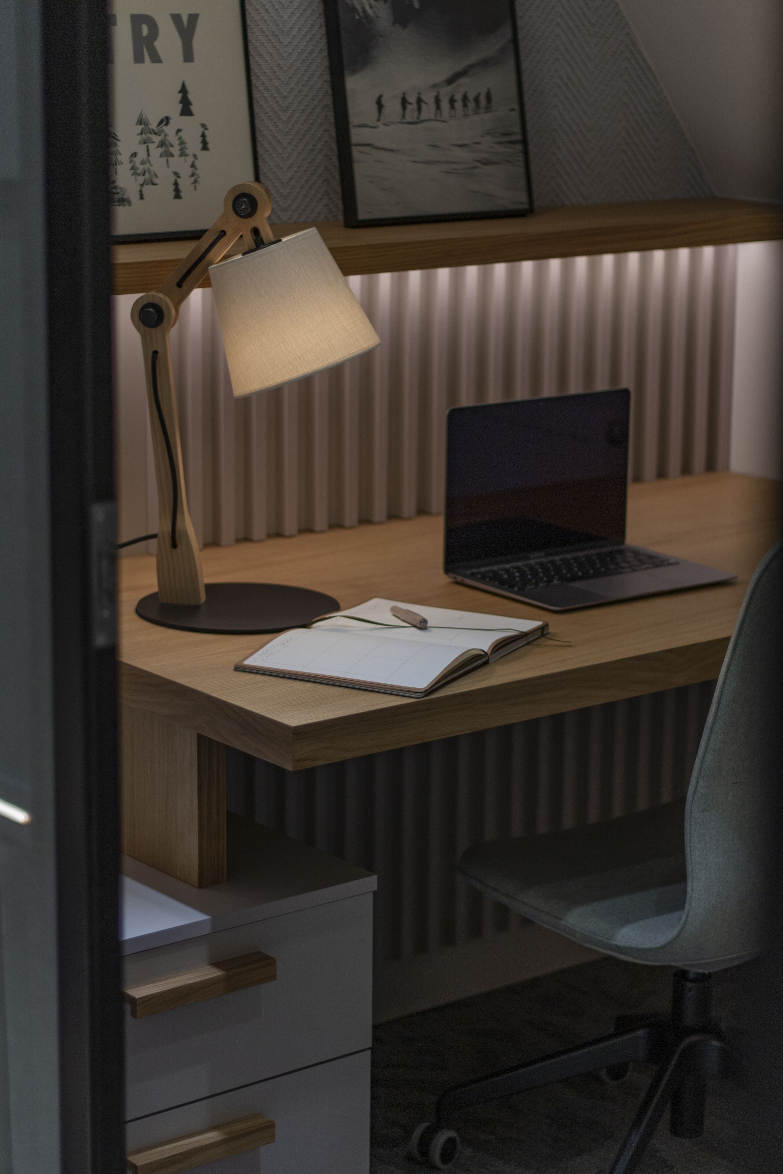 A wooden desk with a laptop, a notebook, and a lamp.
