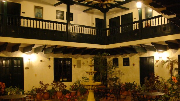 A courtyard with multiple tables and chairs, surrounded by potted plants and a central fountain. - Hotel Hospedería San Carlos Villa de Leyva (Villa de Leyva)