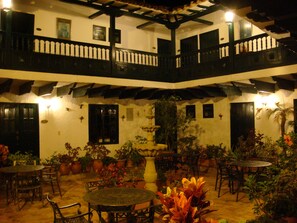 A courtyard with multiple tables and chairs, surrounded by potted plants and a central fountain. - Hotel Hospedería San Carlos Villa de Leyva (Villa de Leyva)