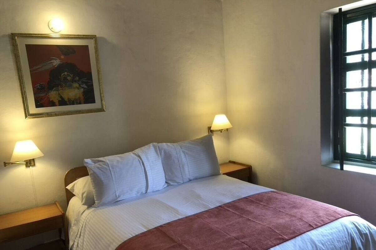 Une chambre à coucher avec un lit, deux lampes de chevet, un tableau encadré au mur et une fenêtre.