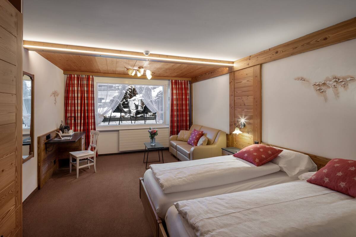 Una habitación de hotel acogedora con dos camas, un escritorio, una silla y un ventanal con cortinas.