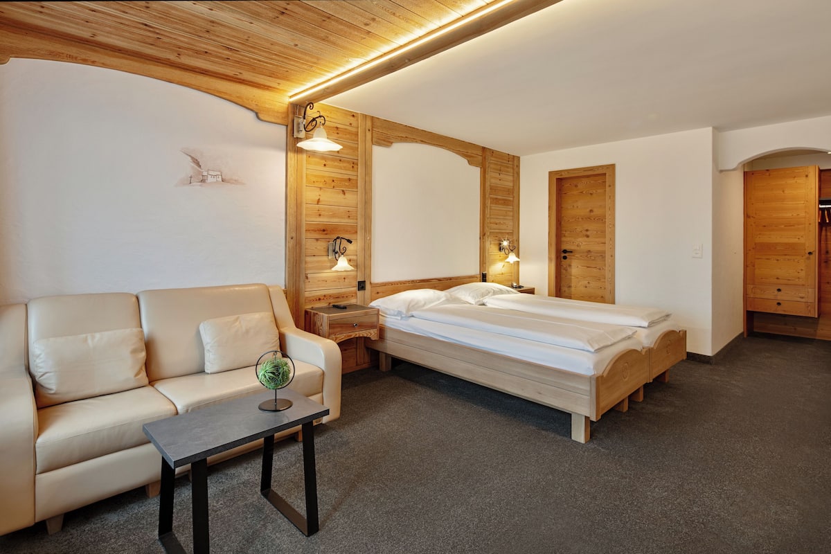 Una habitación con cama, sofá, una mesita y paredes de madera.