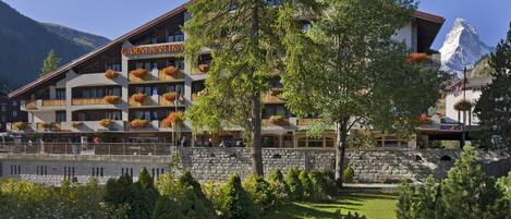 Un hotel con varios balcones decorados con jardineras florales, fachada de piedra y vistas a la montaña.