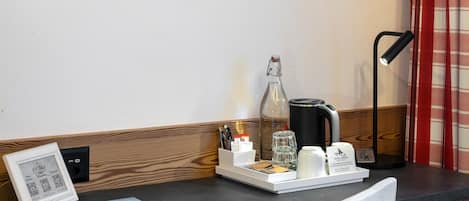 A wooden desk with a coffee maker, a framed picture, and a tray with a cup and a bottle.