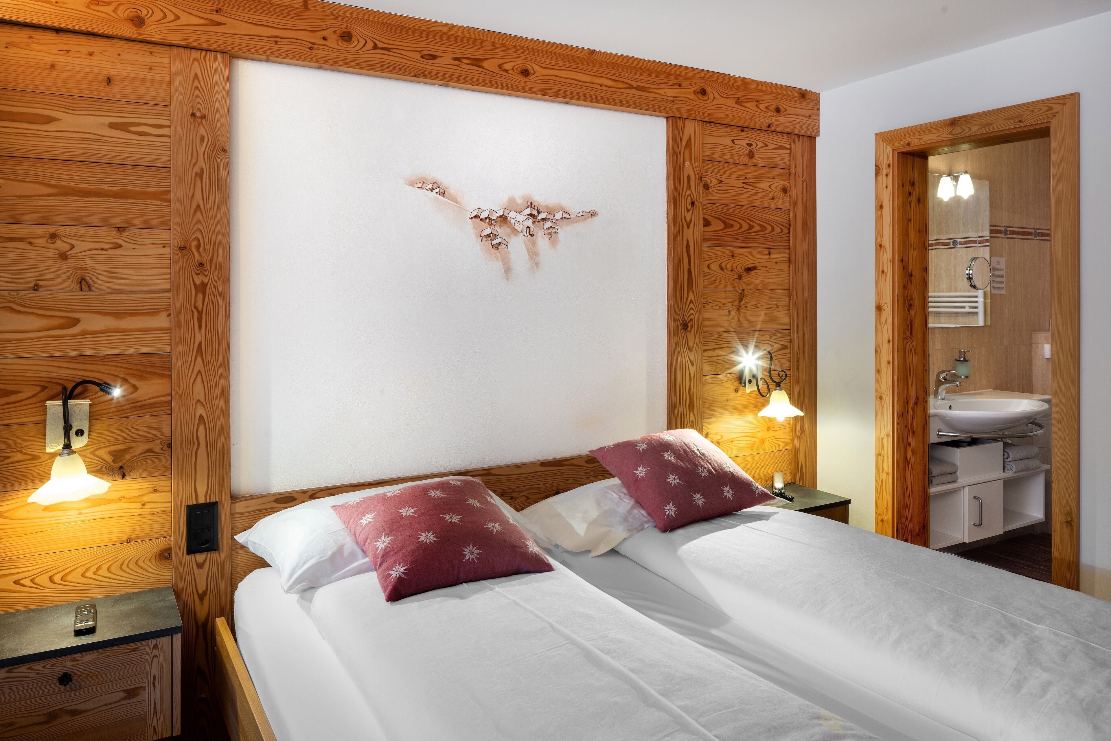 Cama doble con ropa de cama blanca y dos almohadas rojas, cabecera de madera, lámparas de noche y un panel de pared de madera.