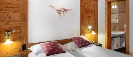 Cama doble con ropa de cama blanca y dos almohadas rojas, cabecera de madera, lámparas de noche y un panel de pared de madera.