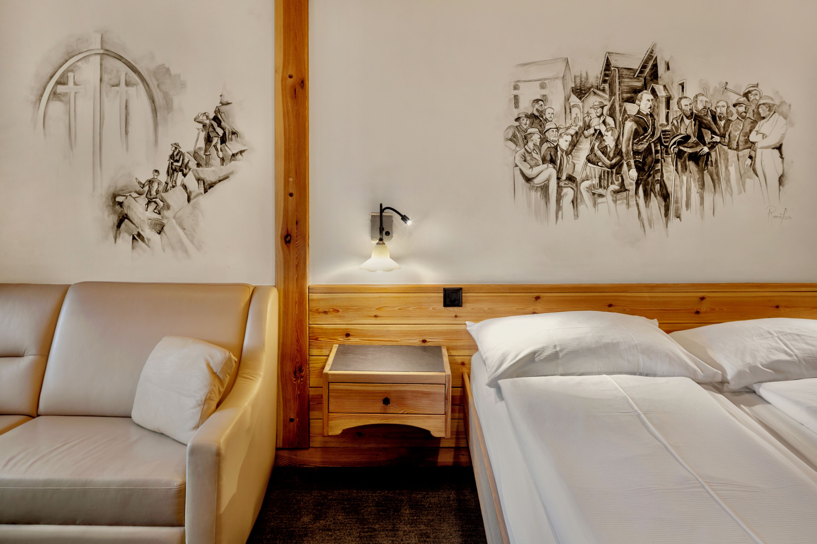 Una habitación de hotel con cabecera de madera, una cama con ropa blanca, una mesita de noche de madera con una lámpara, y un mural en la pared que representa una escena histórica.