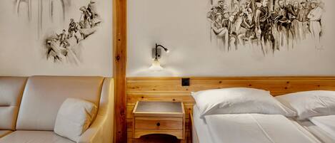 Una habitación de hotel con cabecera de madera, una cama con ropa blanca, una mesita de noche de madera con una lámpara, y un mural en la pared que representa una escena histórica.