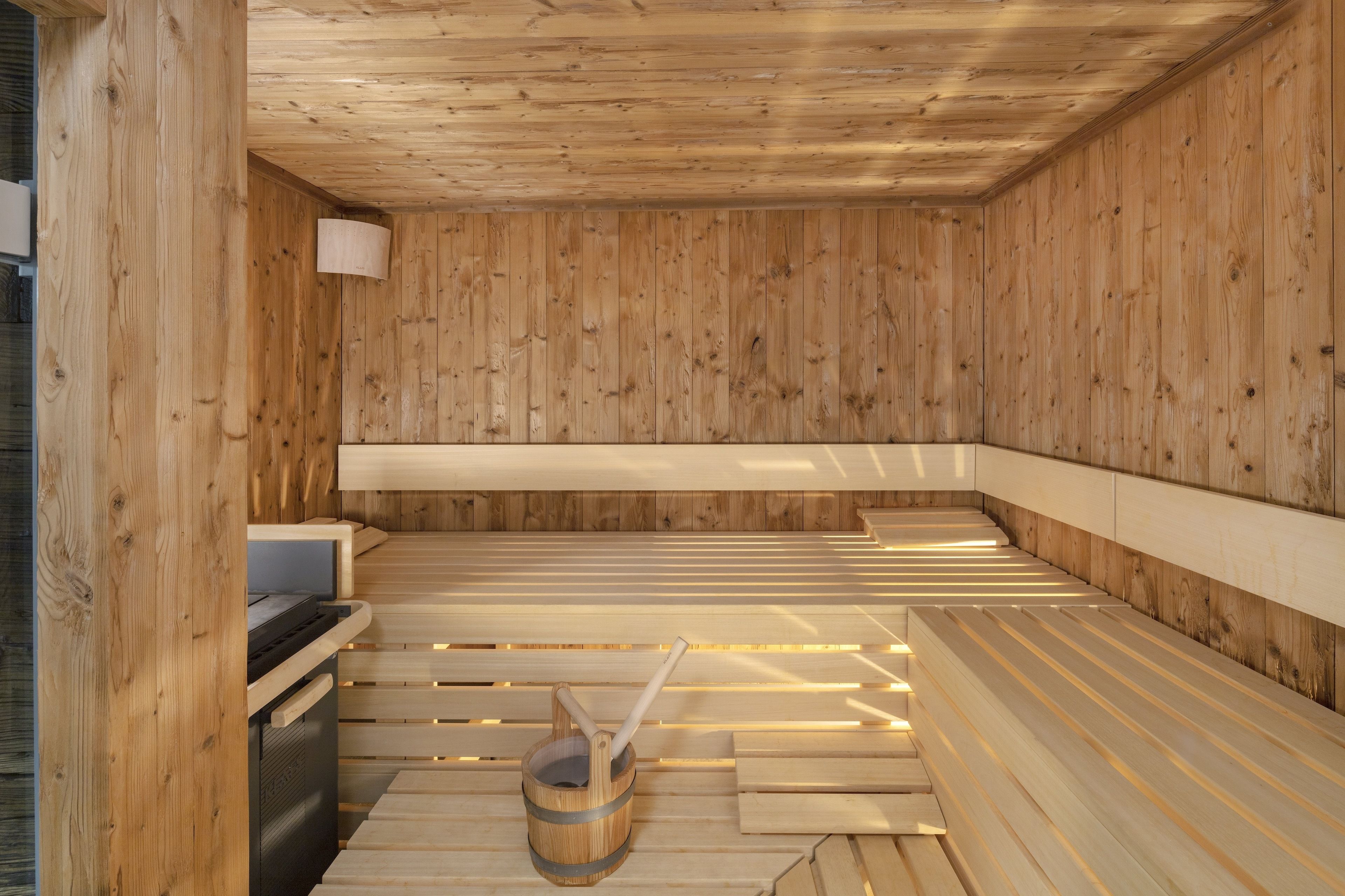 Un sauna avec des bancs en bois et un seau en bois muni d’une brosse.