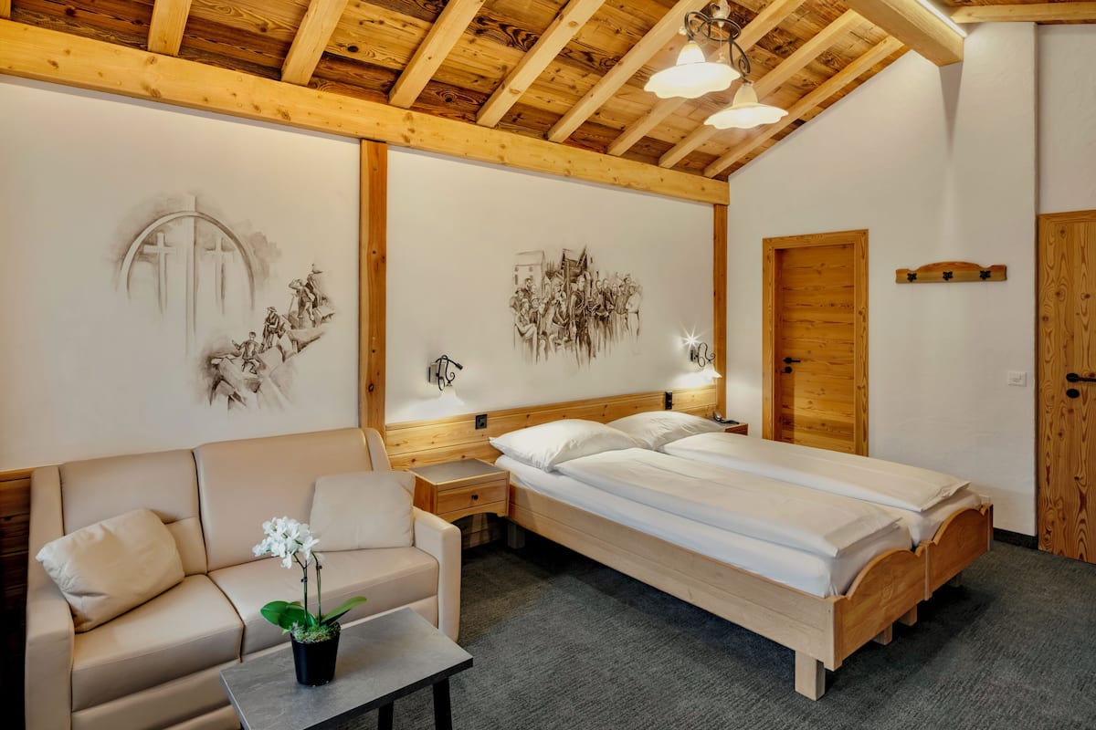 Un dormitorio con techo de madera, una cama, una mesita de noche, una lámpara, un sofá y una pared decorada con obras de arte.