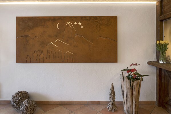A wall with a large abstract painting, a wooden shelf with a vase of flowers, and a decorative pine cone on the floor. - Hotel Antika (Zermatt)