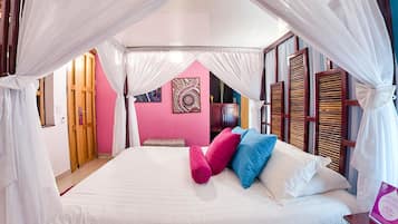 A bedroom with a bed, white curtains, a pink wall, and a wooden headboard.