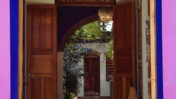 A doorway with a decorative archway, a chandelier, and a tiled floor leading to a room with a large vase.