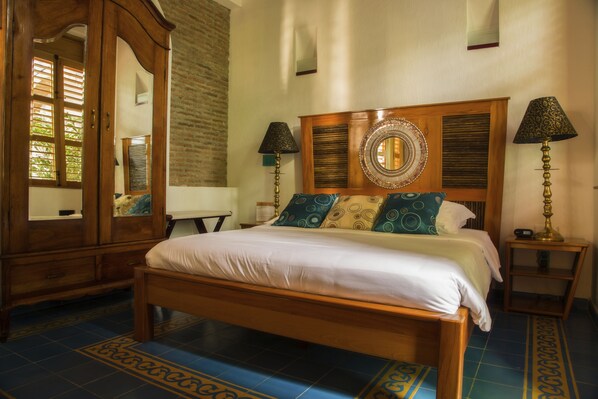 A neatly made bed with a wooden headboard, two bedside tables with lamps, and a large mirror above the bed. - Casa de Isabella, a Kali Hotel (Santa Marta)