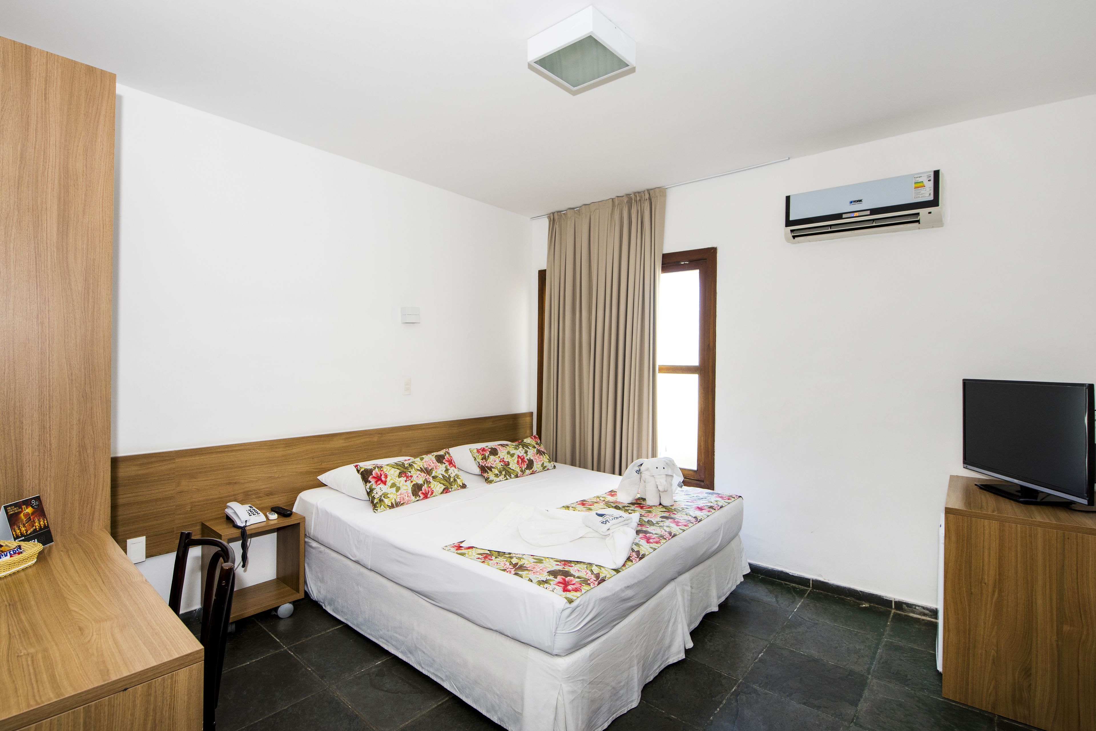 Een hotelkamer met een bed, een bureau, een stoel, een televisie en een airconditioning.