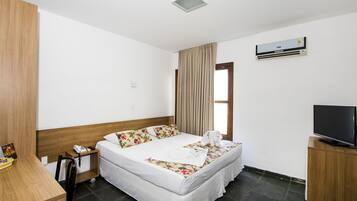 Een hotelkamer met een bed, een bureau, een stoel, een televisie en een airconditioning.