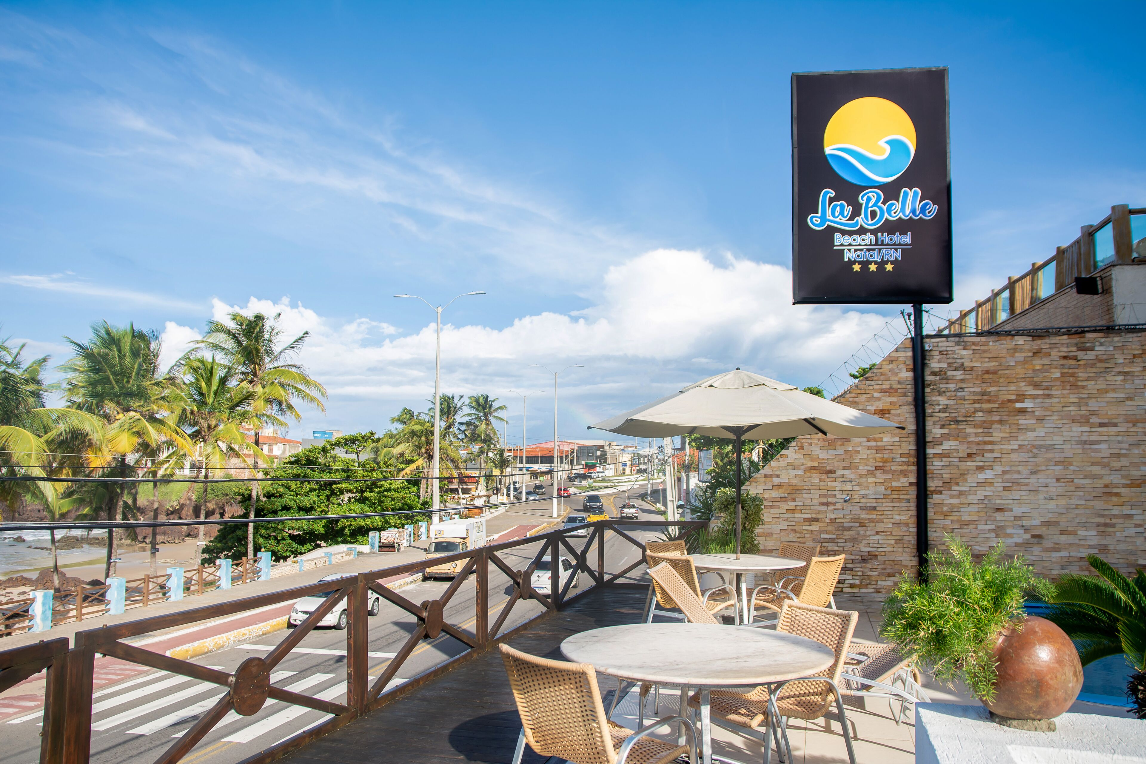 Un patio frente a la playa con mobiliario exterior, palmeras y vista al mar.