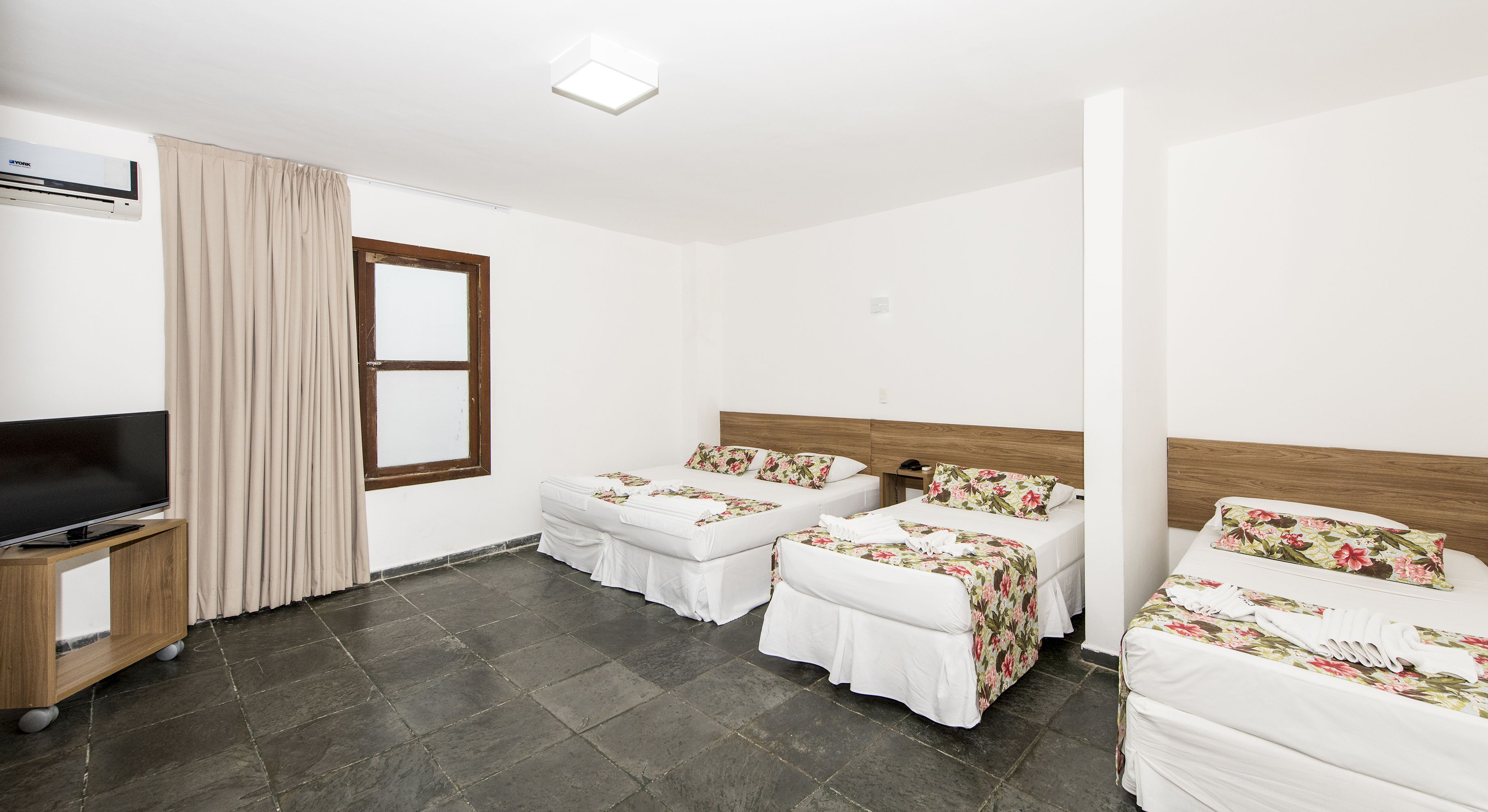 Una habitación de hotel con dos camas individuales, televisión y ventana con cortinas.