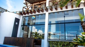 Un edificio moderno con amplios ventanales, una pérgola de madera y una zona de piscina.