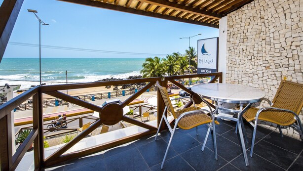 Una terraza con vista a la playa y al océano, que incluye una mesa, sillas, un muro de piedra y un cartel.