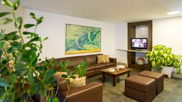 Ein modernes Wohnzimmer mit einem braunen Sofa, einem Couchtisch und einem Fernseher auf einem Schrank. An der Wand hängt ein großes abstraktes Gemälde und rechts steht ein Blumentopf.
