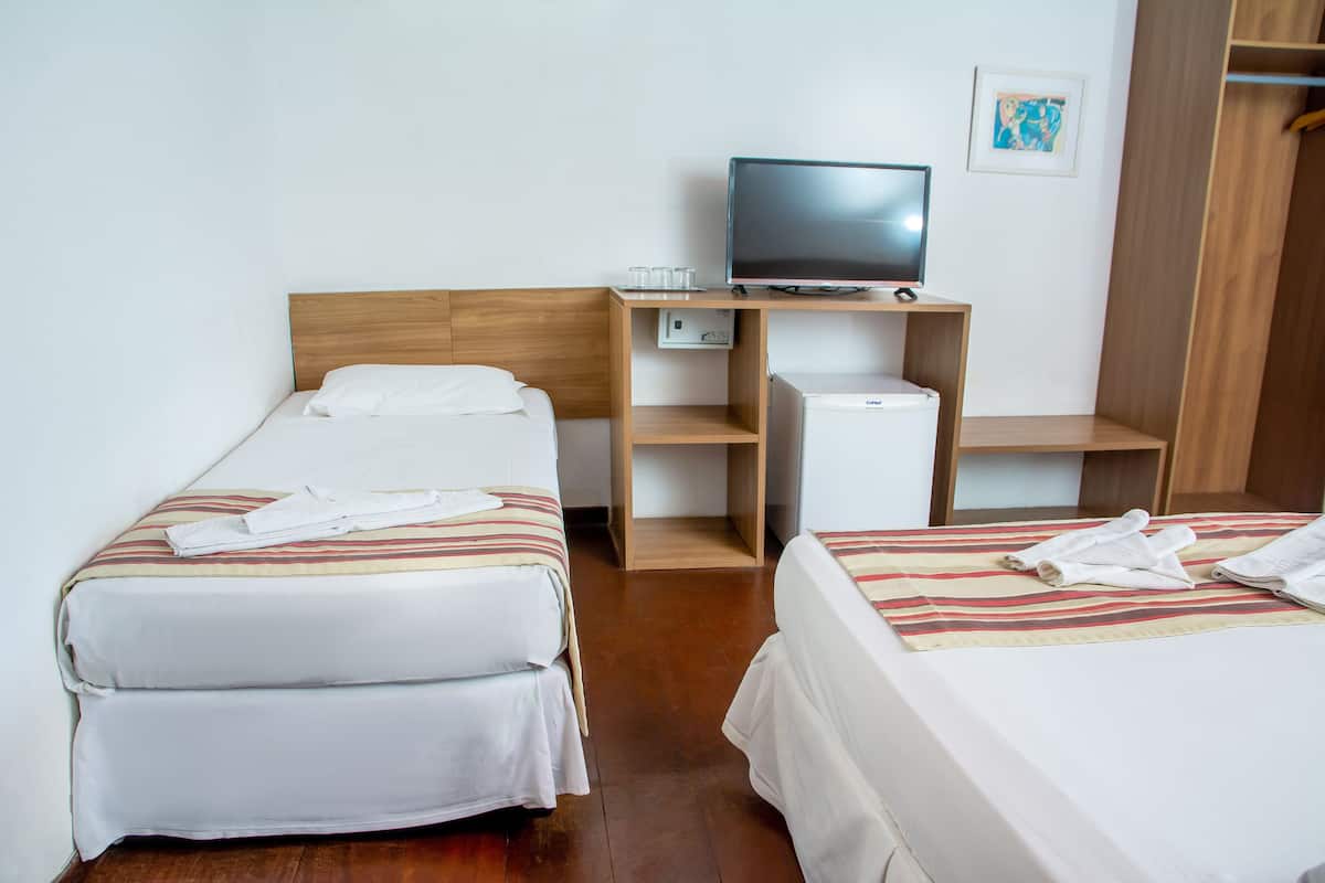 Une chambre d’hôtel avec deux lits, un téléviseur posé sur un meuble en bois, un petit réfrigérateur et un tableau encadré au mur.