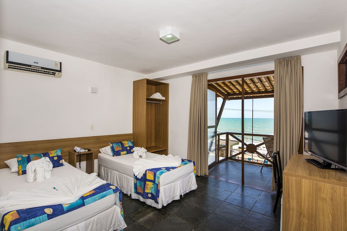 Une chambre d’hôtel avec deux lits, une télévision et un balcon donnant sur la plage.