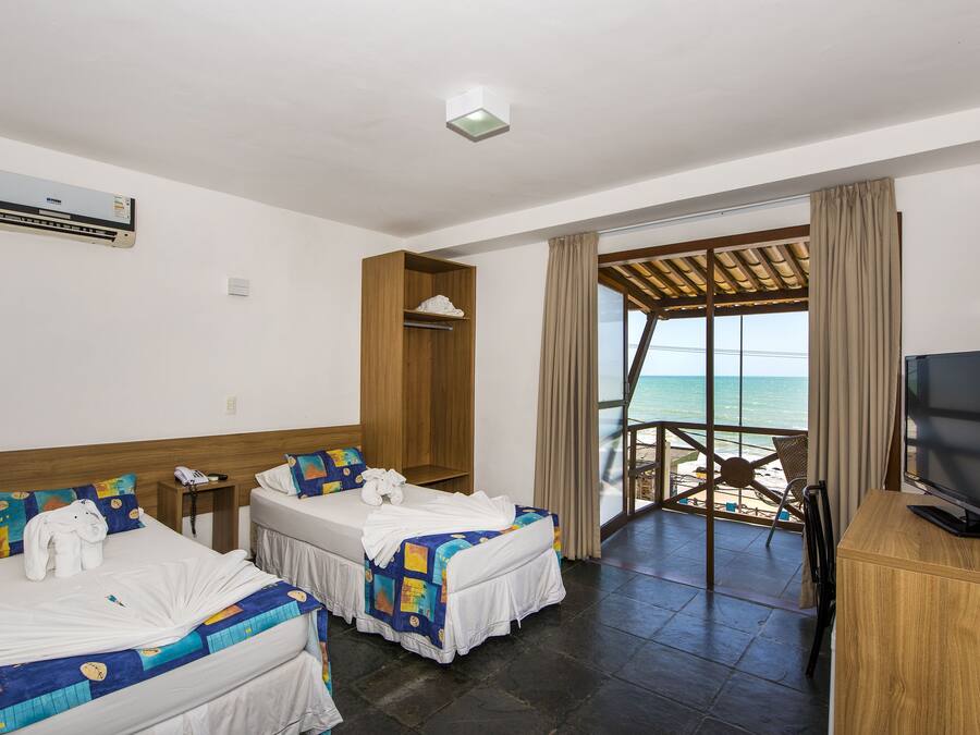 Habitación de hotel con dos camas, televisor y balcón con vista a la playa.