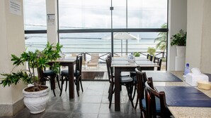 Un restaurante con mesas y sillas, un ventanal grande y una planta en maceta.