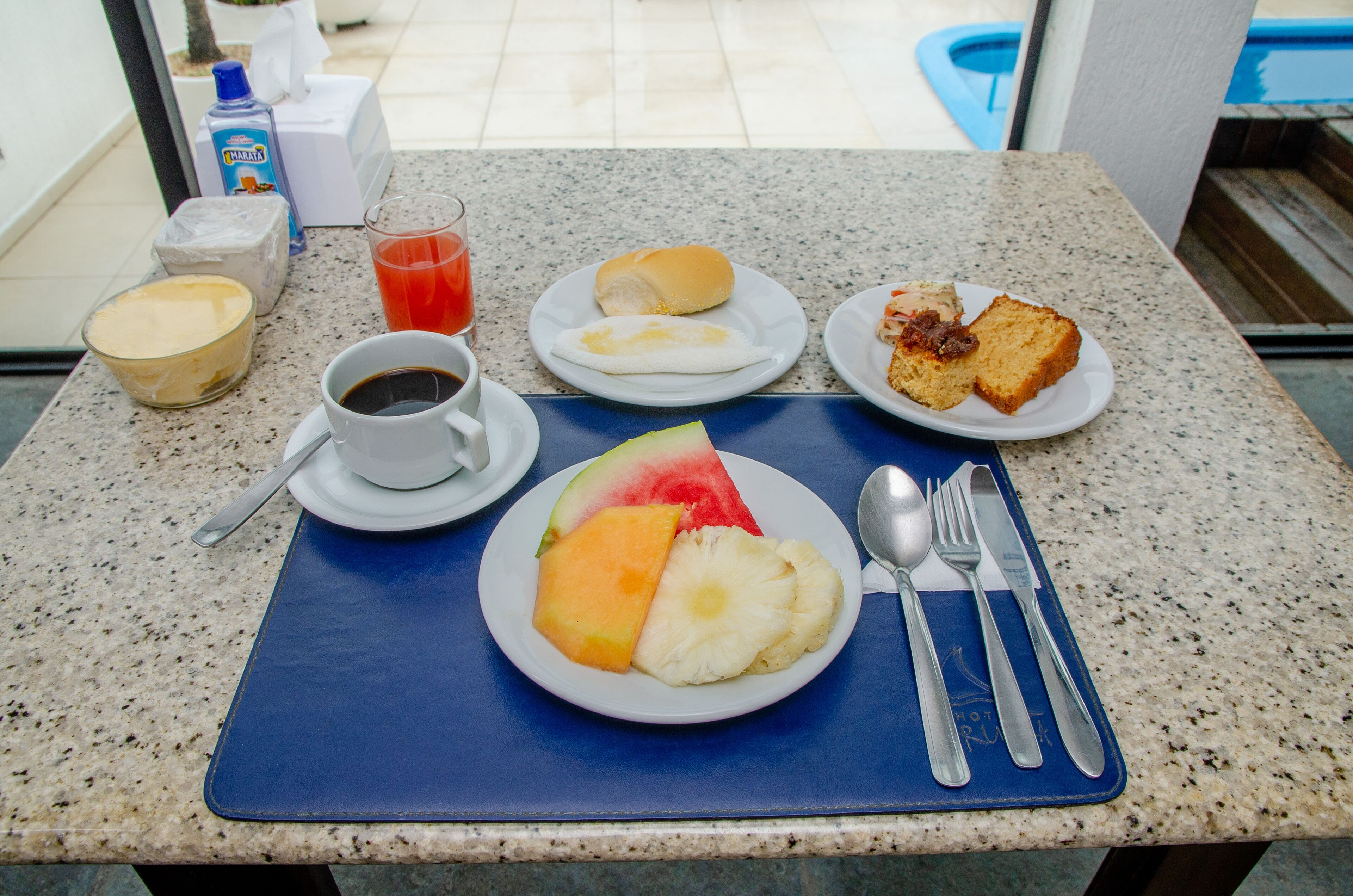A breakfast table with a plate of fruit, a cup of coffee, a glass of juice, and a plate with toast and eggs.