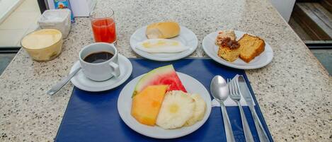 A breakfast table with a plate of fruit, a cup of coffee, a glass of juice, and a plate with toast and eggs.
