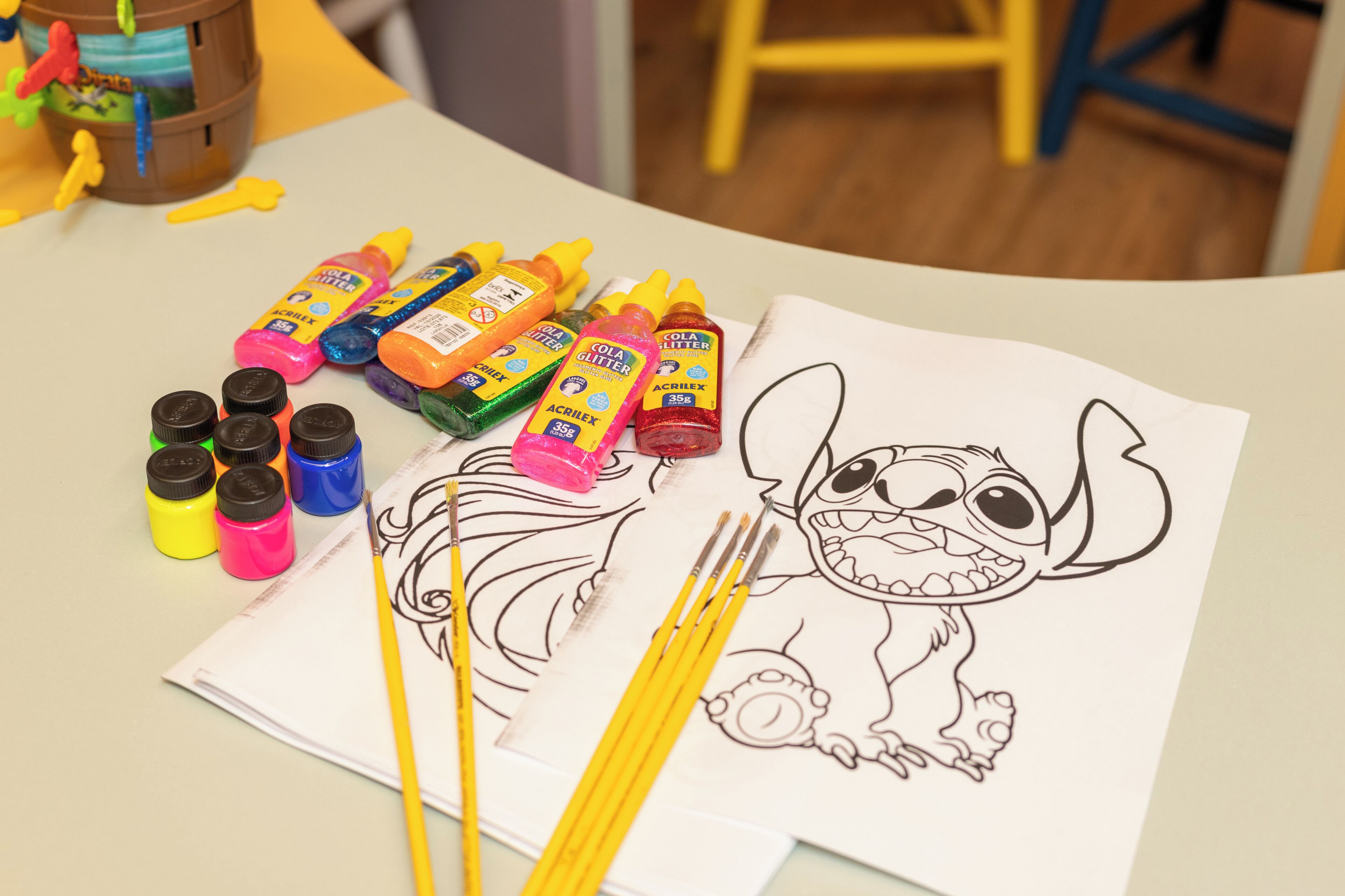 A table with a drawing of Stitch, various colored markers, and paint bottles.