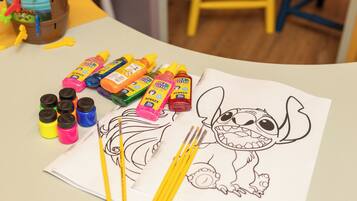 A table with a drawing of Stitch, various colored markers, and paint bottles.