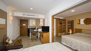 Habitación de hotel con dos camas, un escritorio con televisor, zona de comedor y armario.