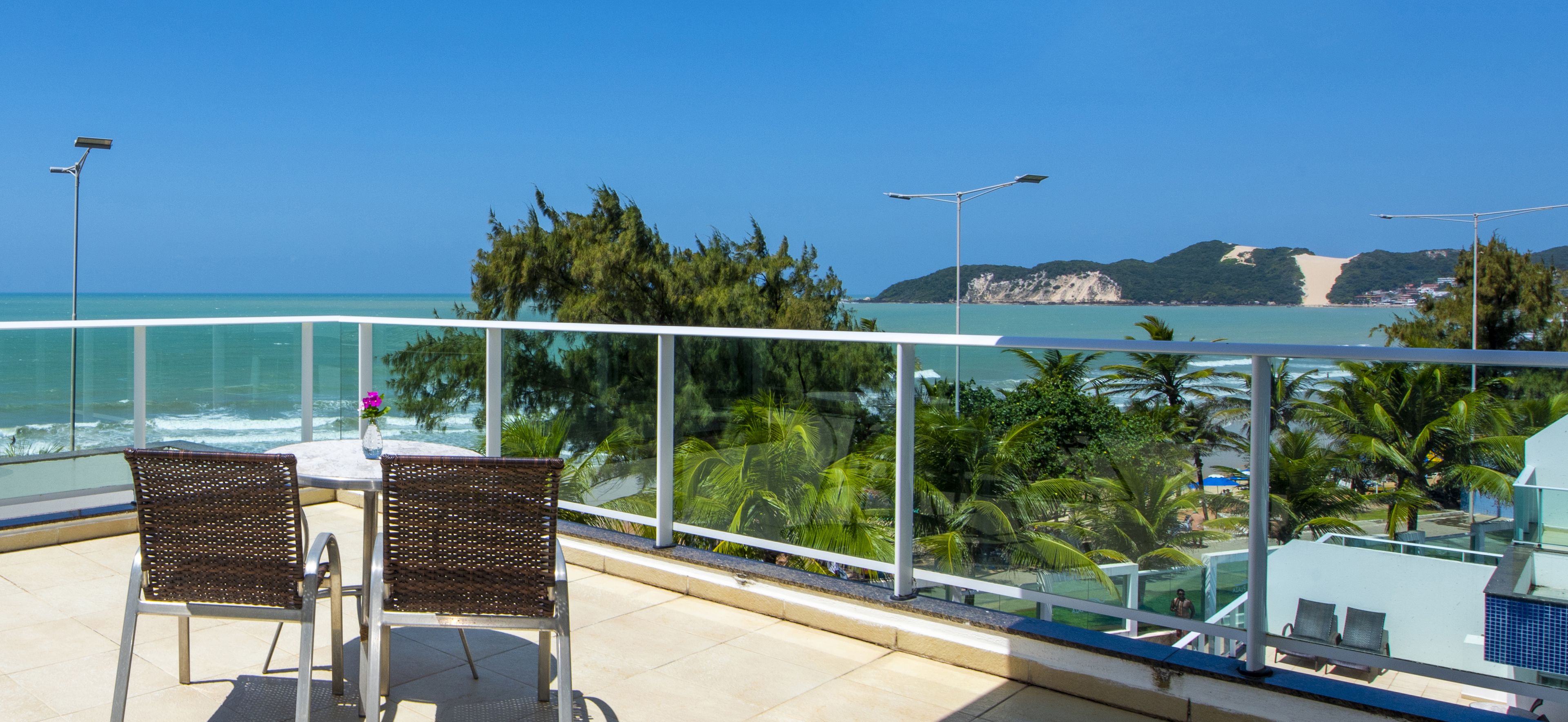 Un balcón con dos sillas de mimbre, una mesa y vista al océano y la playa.