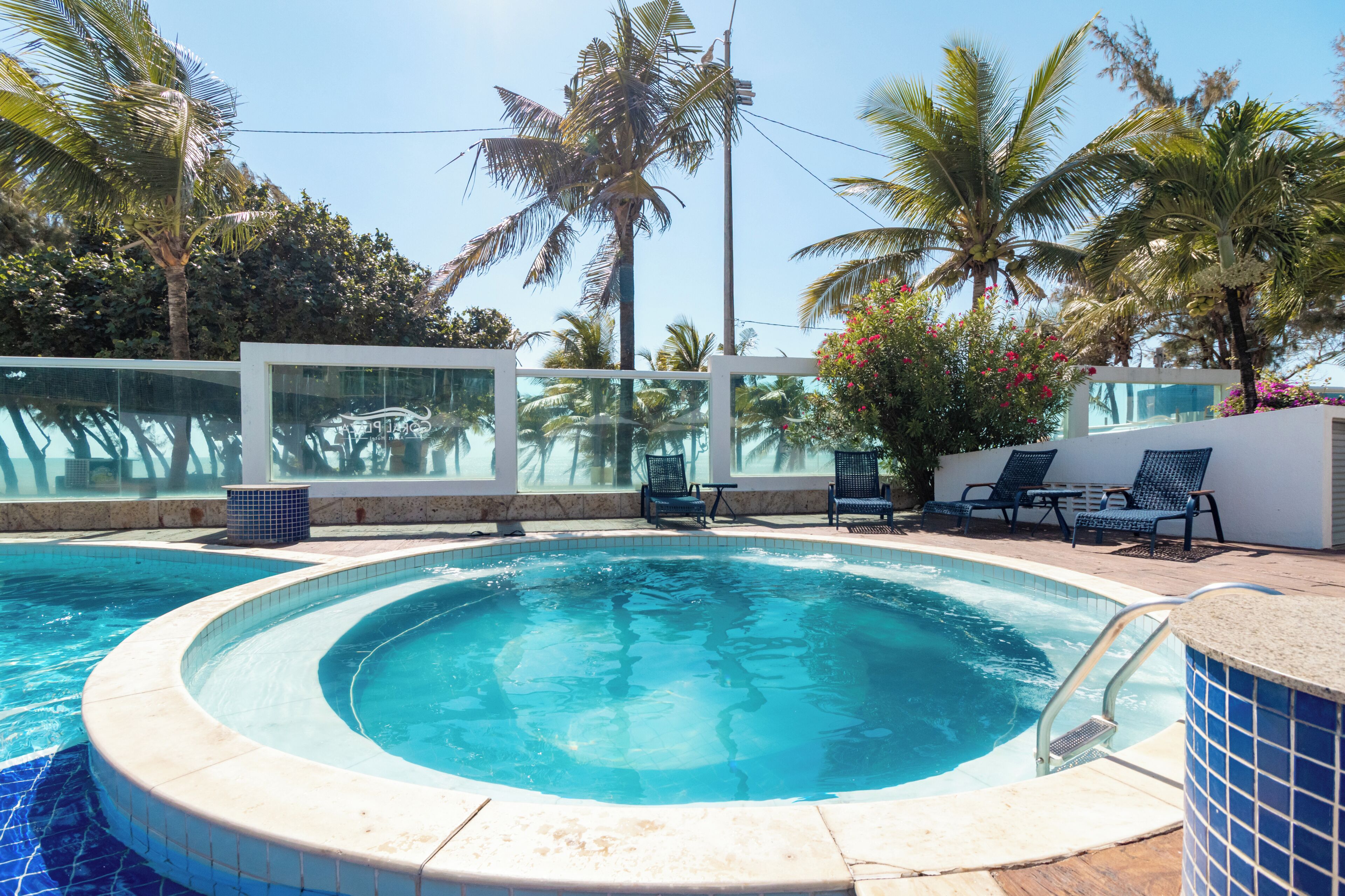 Una piscina con un jacuzzi circular, rodeada de sillas de descanso y palmeras.