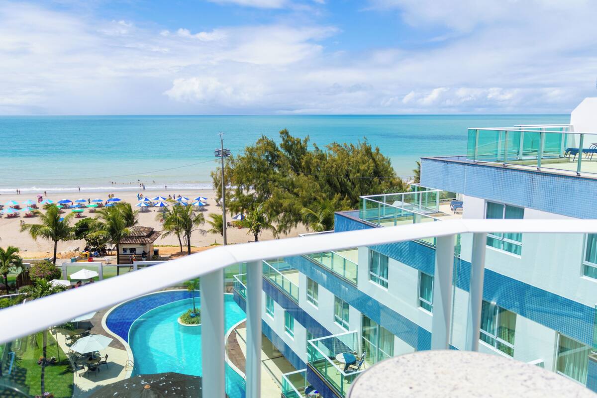 Een hotel met zwembad, uitzicht op het strand en een balkon met zeezicht.