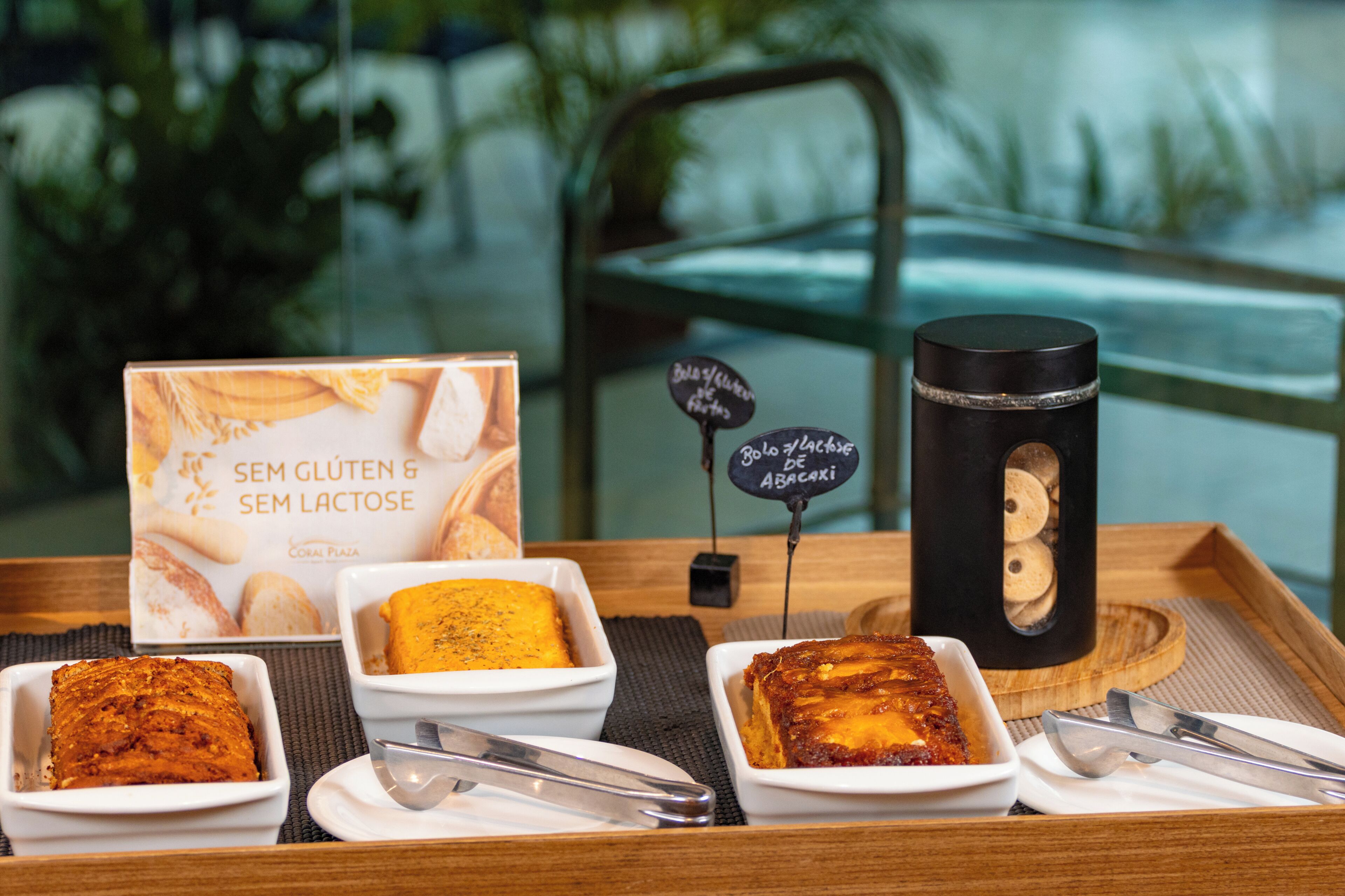 Uma bandeja com sobremesas sem glúten e sem lactose, uma caneca preta e uma placa indicando área sem glúten.