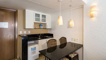 Una cocina compacta con armarios blancos, una encimera negra y una mesa de comedor con sillas de mimbre.