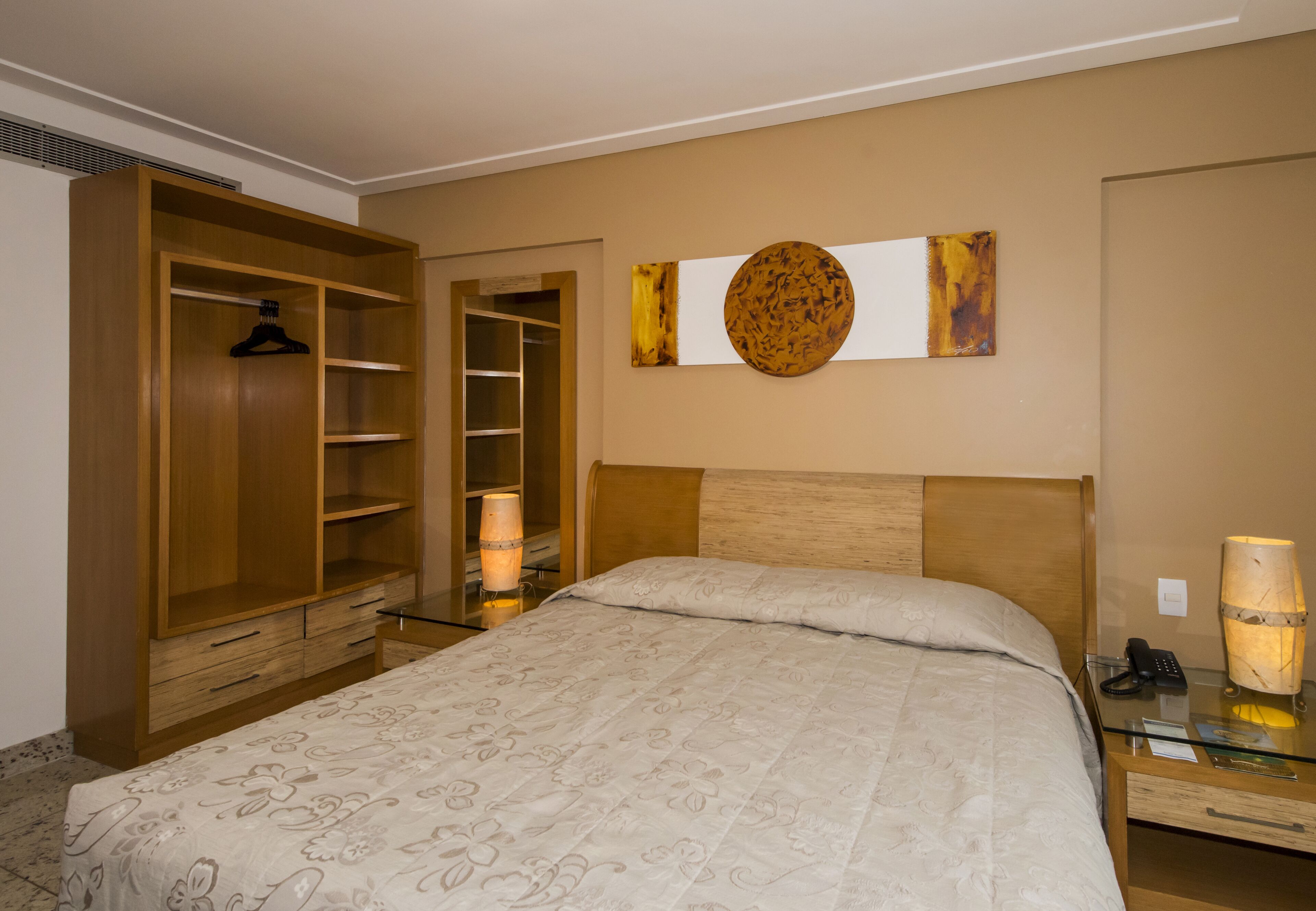 A bedroom with a bed, a wardrobe, a bedside table with a lamp, and a wall-mounted artwork.