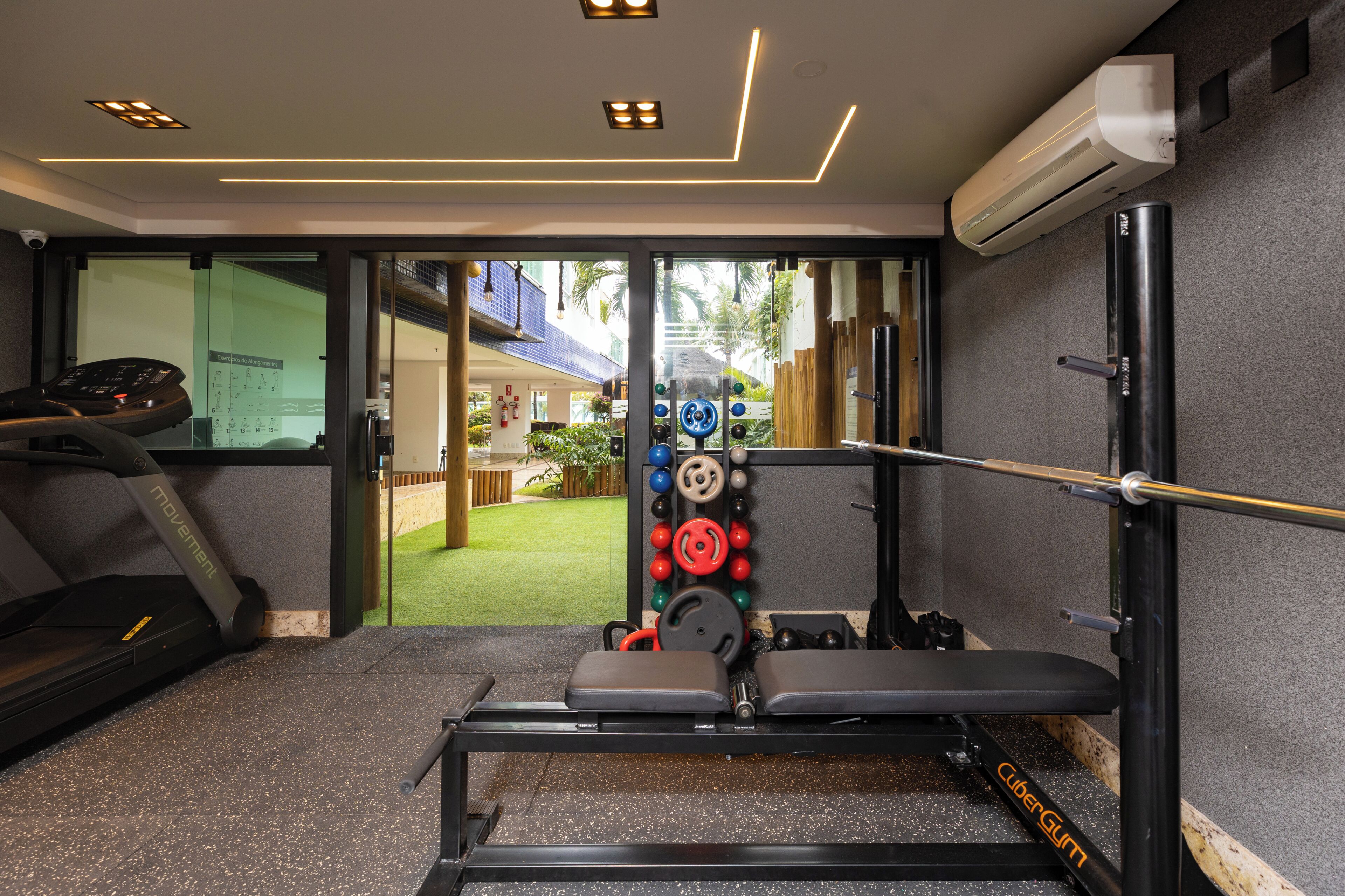 Un gimnasio con cinta de correr, banco de pesas y discos de pesas.