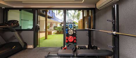 Un gimnasio con cinta de correr, banco de pesas y discos de pesas.