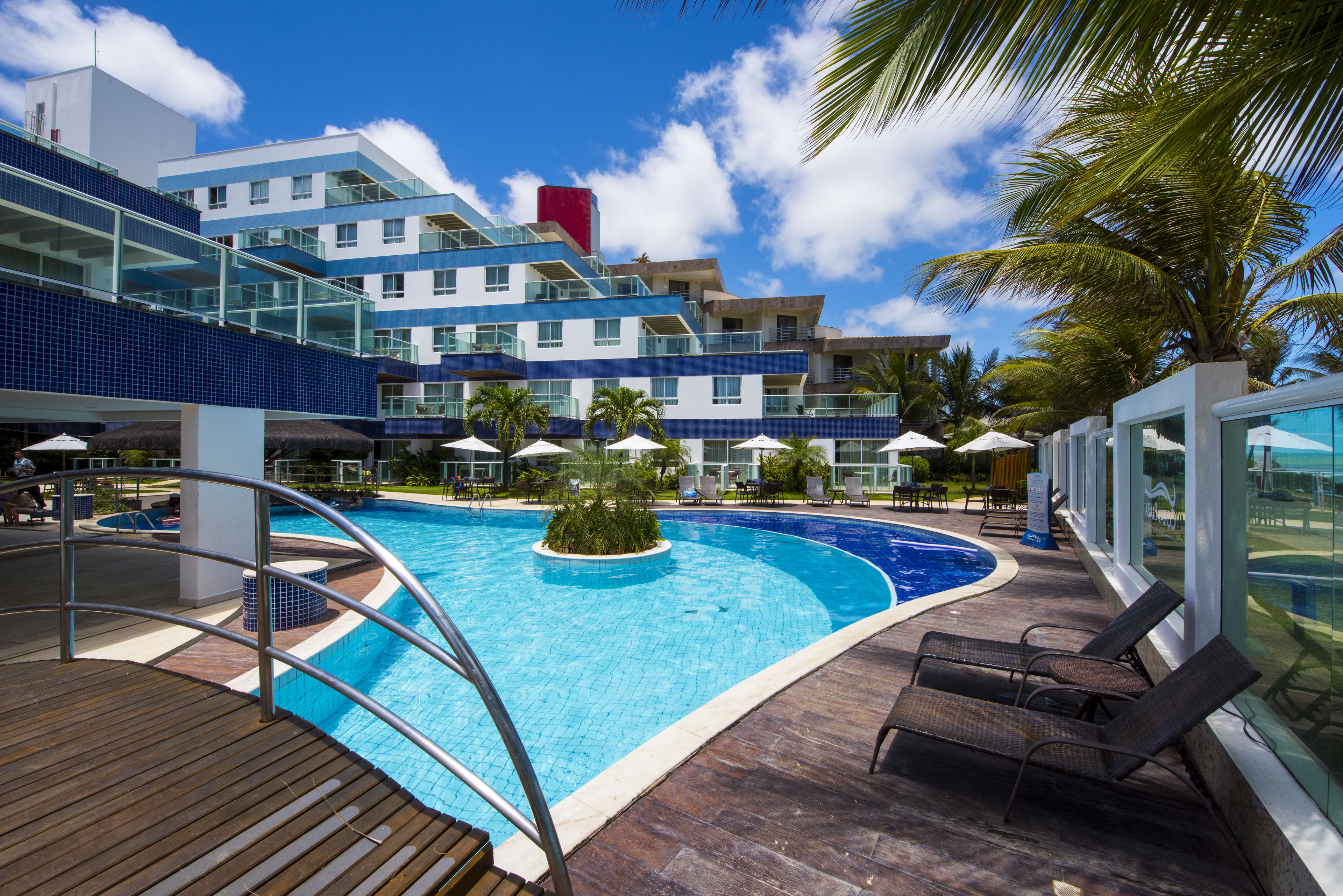 A modern hotel with a large pool, outdoor seating, and a view of the ocean.