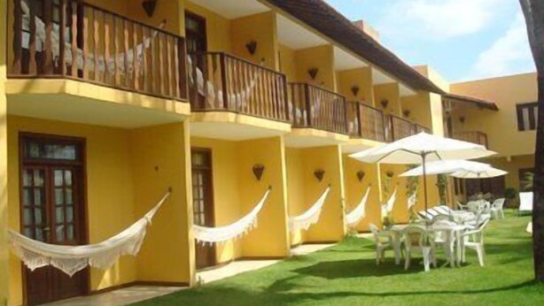Un edificio amarillo de dos pisos con balcones, mobiliario exterior y un patio con césped.