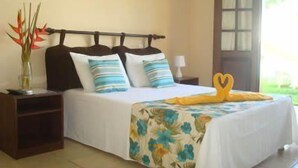 Un dormitorio con cama, mesitas de noche, un jarrón con flores y una ventana con vistas.