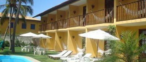 Un hotel con zona de piscina, tumbonas y sombrillas.